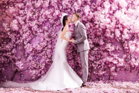 Fun purple flower wall at wedding, bride and groom kissing