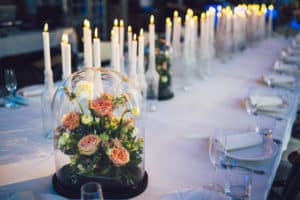 Pink flowers nestled under a glass dome on a long dinner table with candles