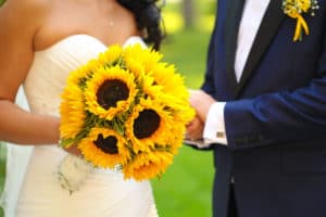 Bride holding sunflower bouquet and groom wearing sunflower boutonniere