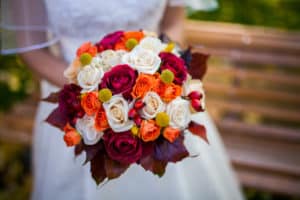 Bride holding autumn wedding bouquet with red, white, and orange roses