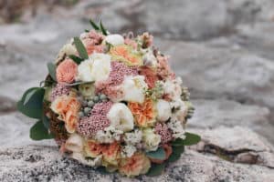Bridal bouquet on the rock. Bridal bouquet of natural flowers. Flowers on a gray big stone. Wedding rings. Natural flowers. The morning of the bride.
