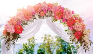 Beautiful white wedding arch decorated with pink and red flowers outdoors