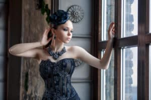 Portrait of an elegant girl in a chic necklace and hat in a gothic interior.
