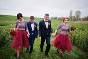 Groomsmen and bridesmaids running in blackcurrant field on a wedding day.