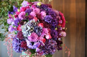Round flower arrangement in silver stand with purple, pink, and magenta flowers, dahlia, rose, and hydrangea.