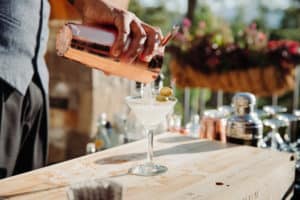 A bartender mixes and pours a martini into a martini glass at an outdoor bar with lots of sunlight
