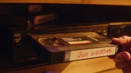 Close Up of a Person Inserting a VHS Cassette in a Player with Nostalgic Wedding Footage from Home Video Camera. Retro Nineties Technology Concept. Old VCR with Shallow Depth of Field and Bokeh.