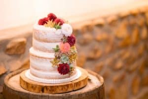 A beautiful white wedding cake decorated with colorful flowers on a wooden barrel