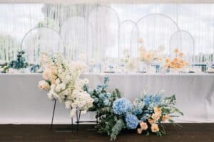 Outdoor banquet and modern design for wedding ceremony in summer. Linen tablecloth, candles, flowers and accessories, glasses and plates on table for guests with chairs, flat lay, nobody