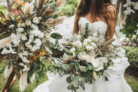 Woman holding in hands big wedding bouquet in Boho style. Dried flowers, white roses and orchids, bird feathers in decor. Floristic concept.