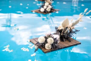 A wooden raft with a bouquet of dried flowers and candles floats in a pool of blue water. Wedding decorations.