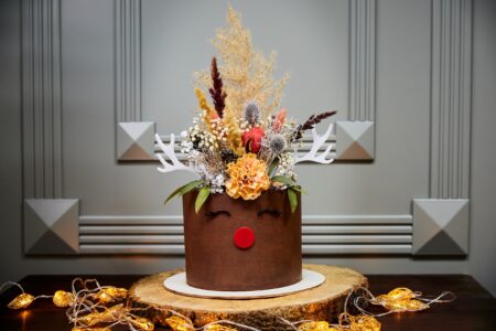 Christmas Banana Cake with Vanilla cakes, Cream Cheese and Salted Caramel on the background of candles, garlands, fir branches and cones