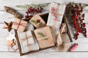 Flat lay of a wood box filled with Christmas presents surrounded by wrapping tools and supplies both natural and man made.