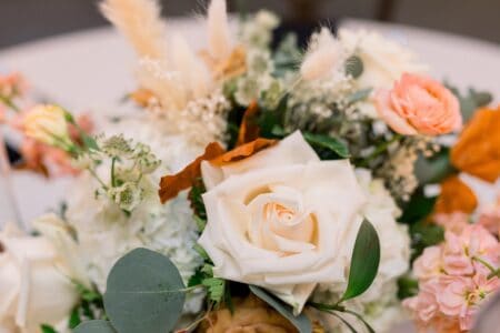 A close-up of a bridal bouquet with white roses and greenery and pink and peach flowers