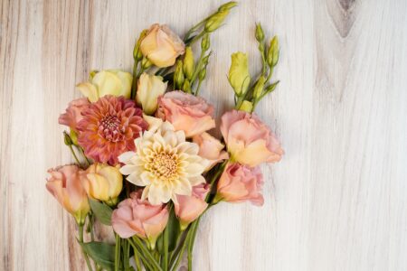 Bouquet of lisianthus flowers and two dahlia flowers. Light wood background. Peach and cream colors. Space for text. Romantic.