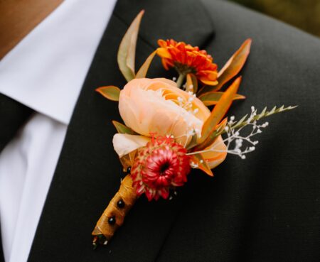 Close-up of a groom's lapel with an elegant boutonniere featuring a peach rose and orange accents